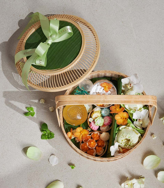 Woven bamboo basket filled with lotus flowers, orchids, decorative sweets, and aromatic elements with green ribbon