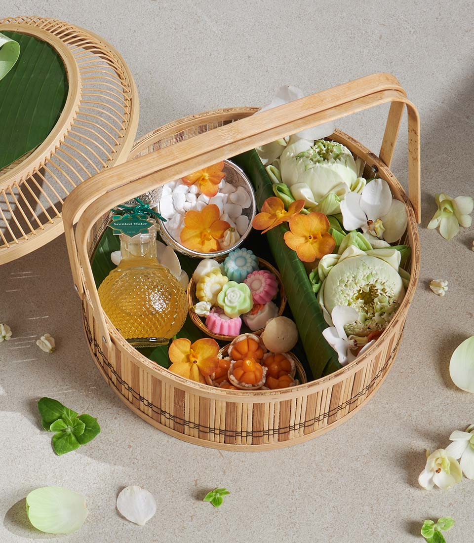 Bamboo woven gift basket with scented water, lotus buds, orchids, and pastel flower sweets for thoughtful gifting