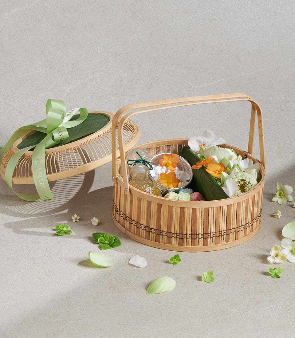 Bamboo gift basket with lotus flowers, golden mist bottle, and white pebbles on neutral background