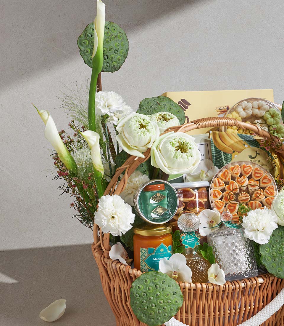 Luxury wicker gift basket with white lotus flowers, calla lilies, gourmet treats, and artisan beauty products in gold and