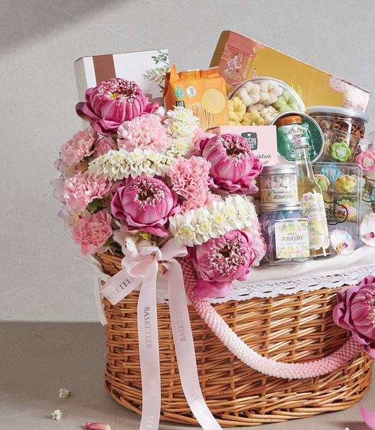 Woven wicker Songkran gift basket with pink lotus flowers, carnations, gourmet treats, and artisan snacks