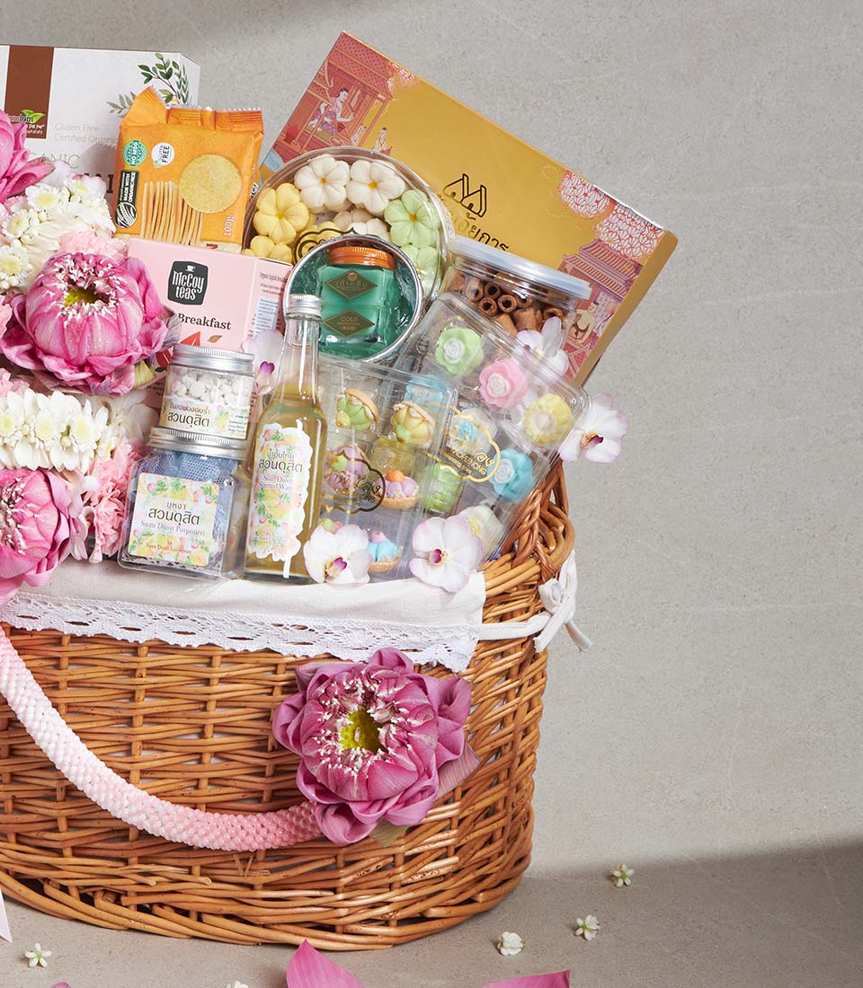 Woven wicker gift basket with pink lotus flowers, gourmet teas, artisan cookies, and Thai treats for Songkran celebration