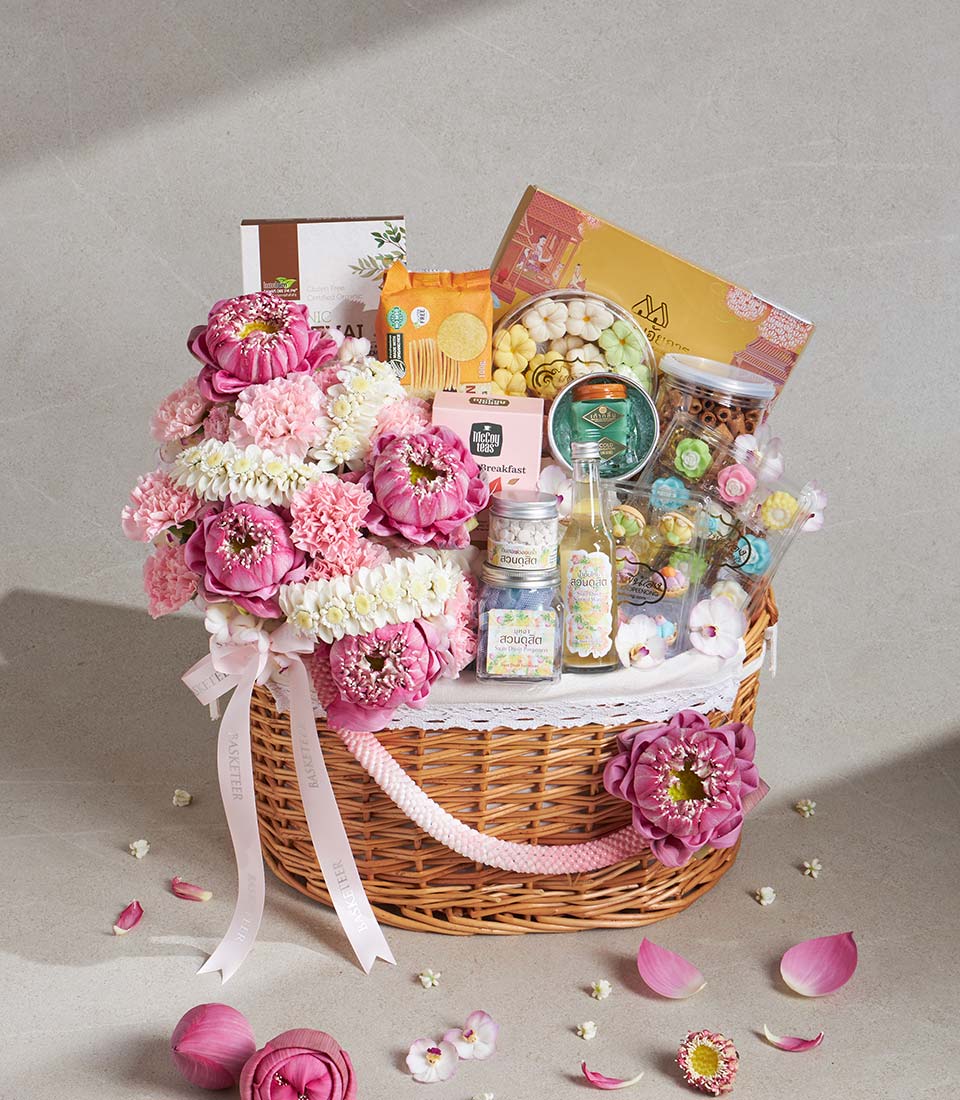 Luxury gift basket with pink lotus flowers, white blooms, and gourmet treats in wicker lined with lace