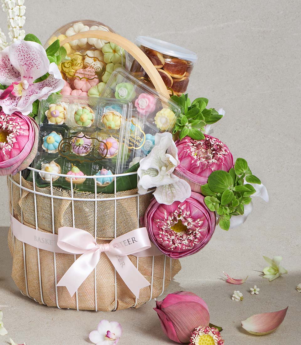 White wire gift basket with Thai desserts, pink lotus flowers, and white orchids tied with silk ribbon