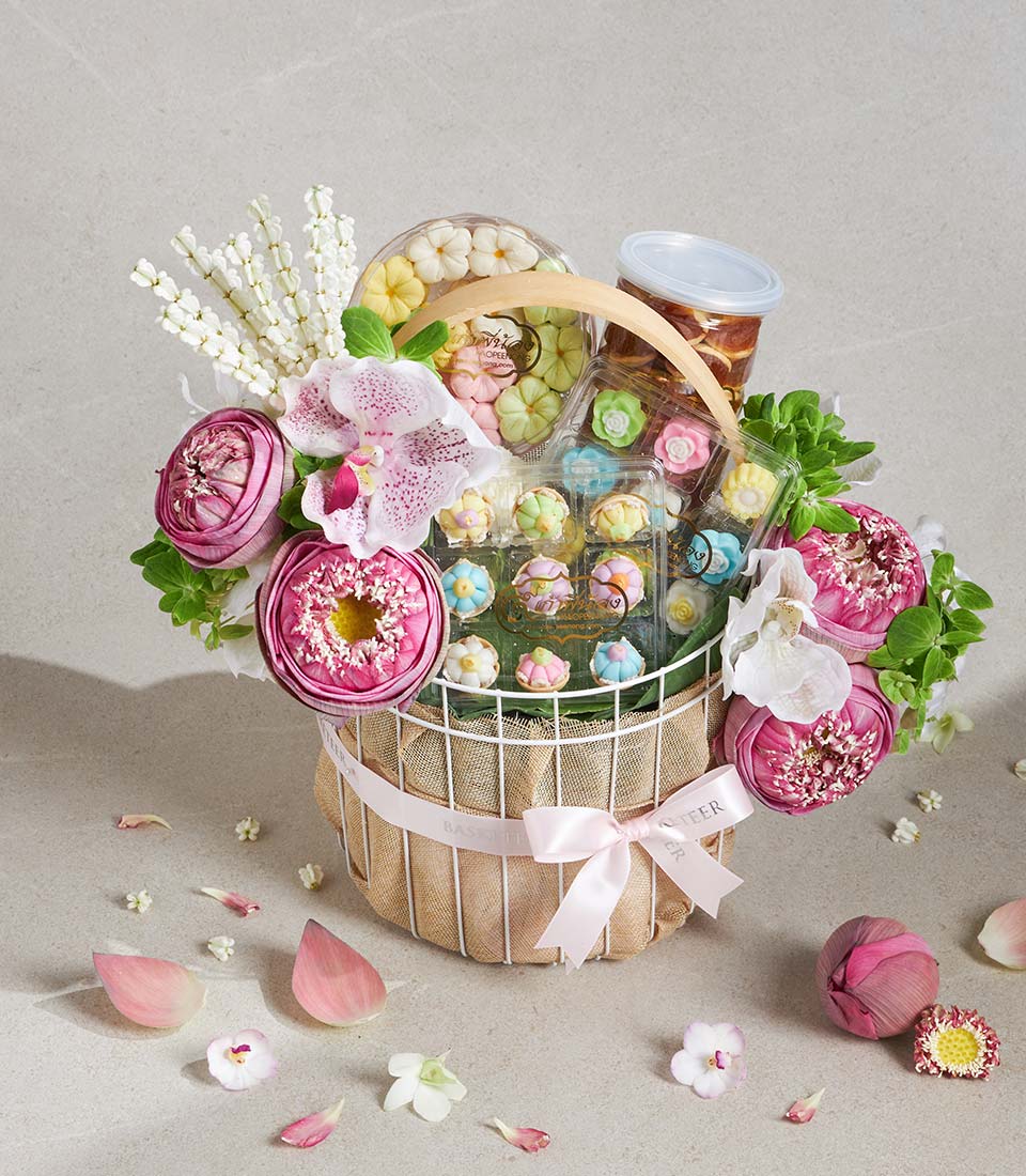 Luxury gift basket with fresh pink lotus flowers, orchids, and artisan Thai pastries in pastel hues, tied with pink satin