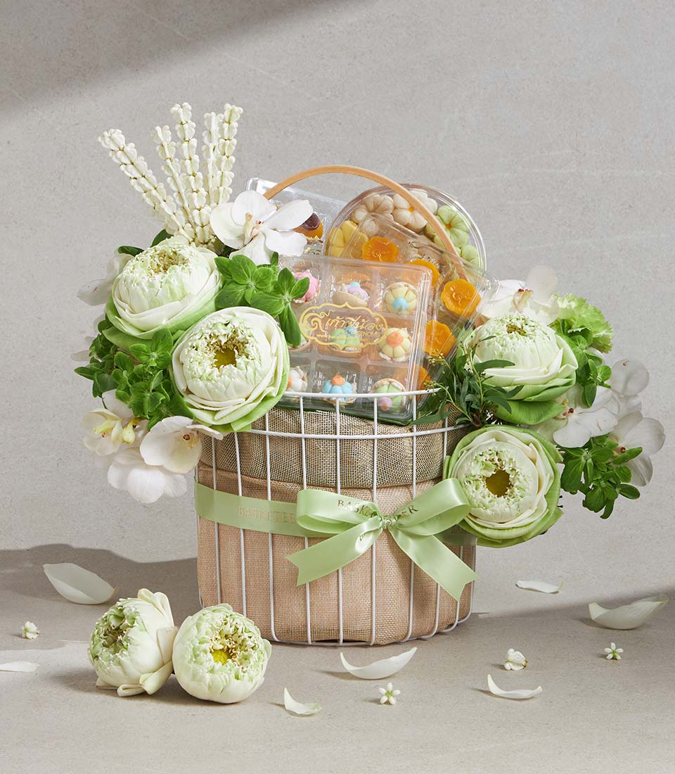 White lotus and orchid gift basket with pastel flower confections and miniature cakes, tied with light green ribbon