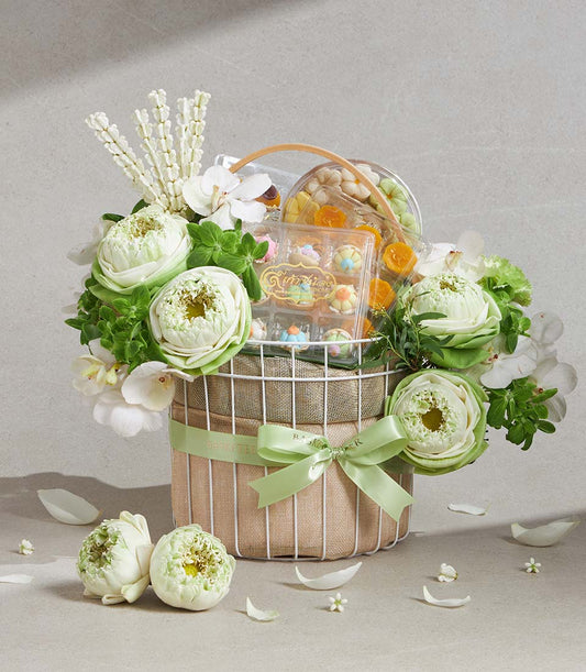 White lotus and orchid gift basket with pastel flower confections and miniature cakes, tied with light green ribbon
