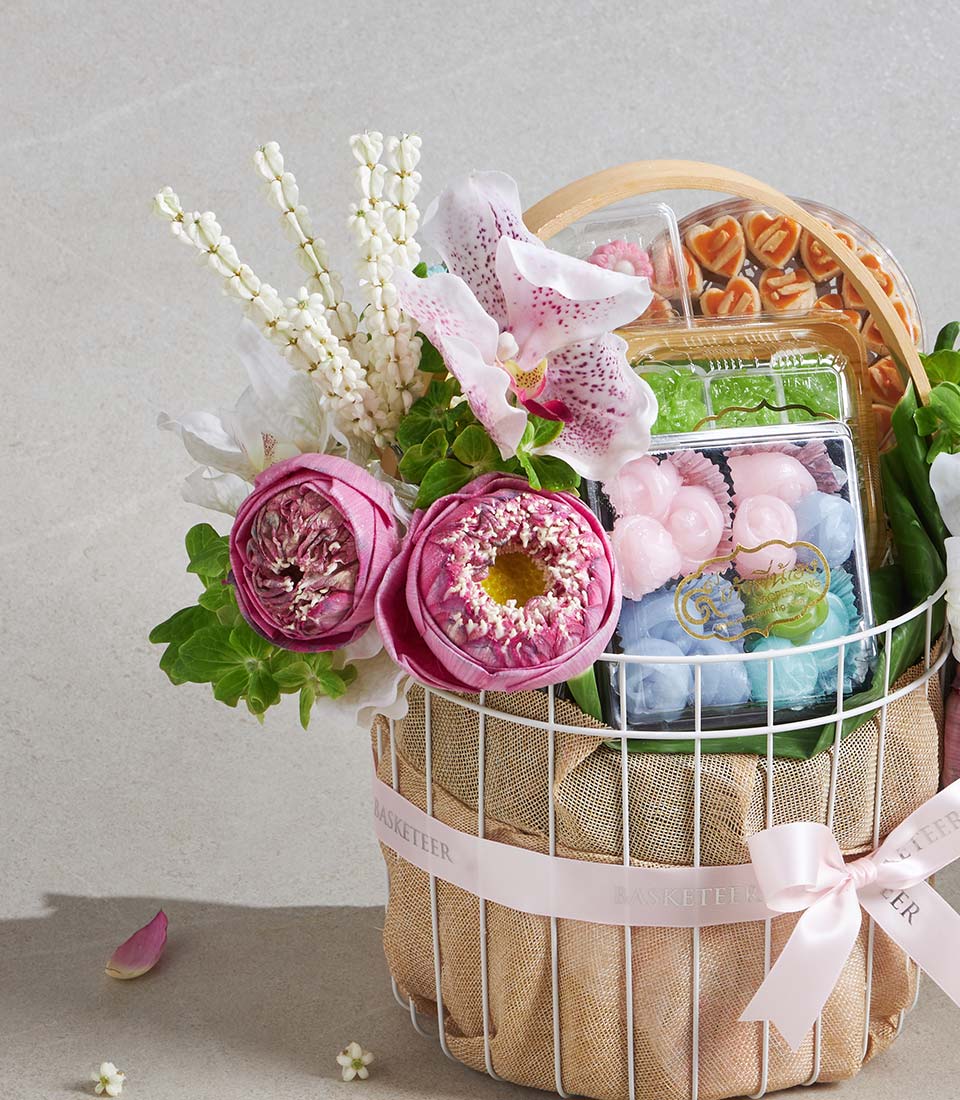 White wire gift basket with pink lotus flowers, white orchids, and assorted Thai sweets in clear containers
