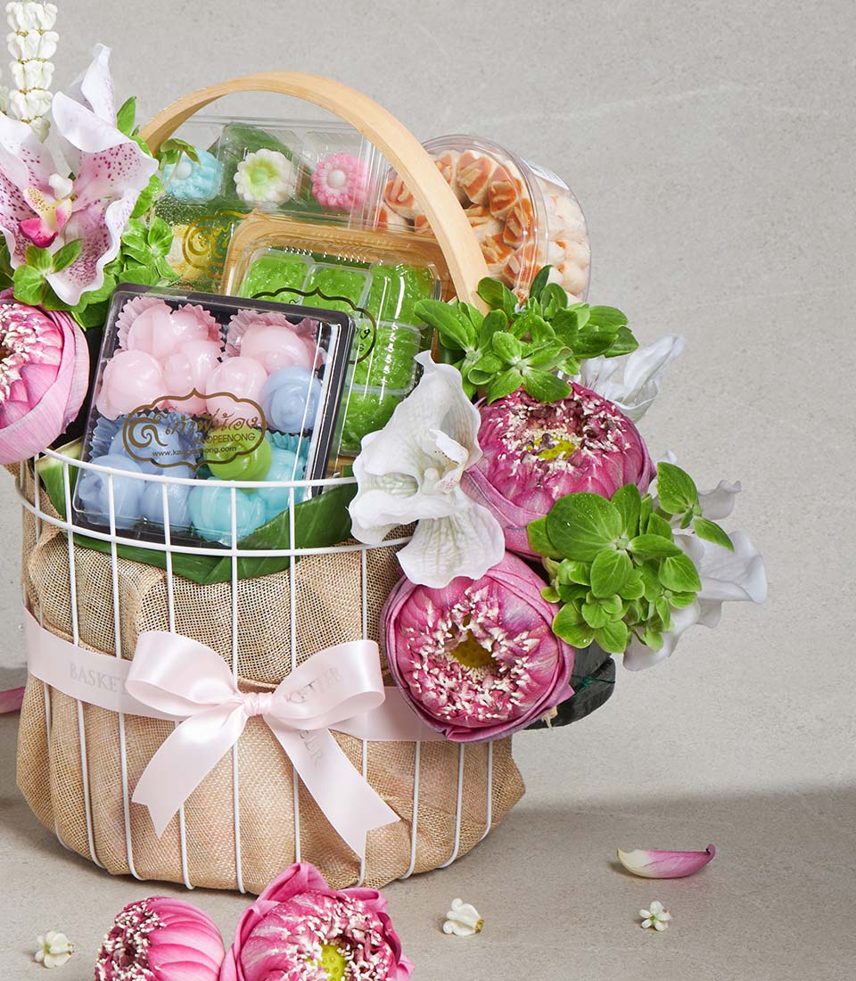 Songkran lotus blessing gift basket with pink and white flowers, confections, and pastries in burlap wrap with pink satin bow