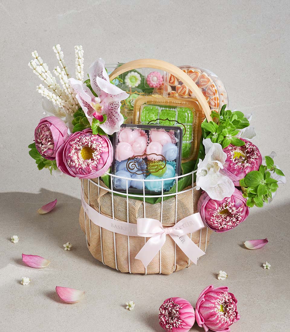 Luxe white wire gift basket with pink lotus flowers, white orchids, and gourmet sweets in pastel containers, tied with pink