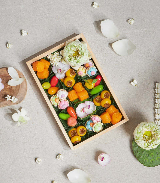 Wooden box of vibrant Thai lotus and jasmine desserts in banana leaf cups with fresh white flowers