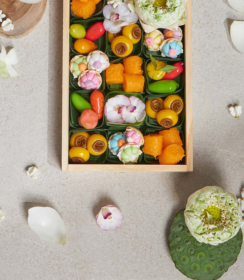Thai lotus sweet dessert mini box with colorful flower-shaped candies, fruit sweets, and golden confections in green leaf