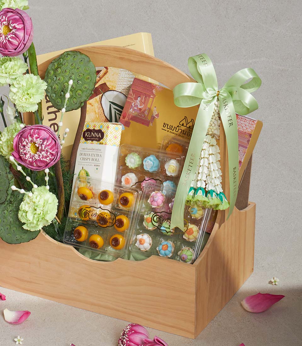 Light wooden gift basket with Thai sweets, durian rolls, and flower-shaped candies, tied with green satin ribbon and Thai