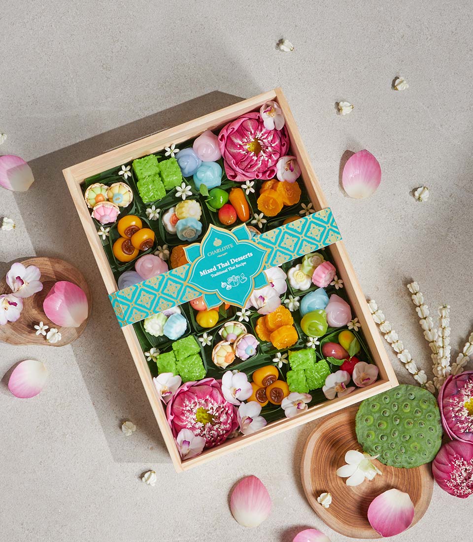 Wooden box of colorful Thai desserts in flower and fruit shapes with teal ribbon and orchid garnish