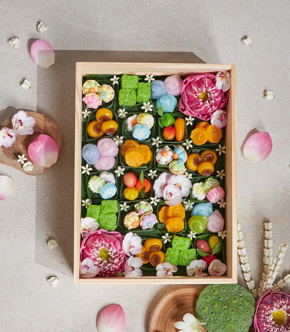 Wooden gift box of colorful Thai lotus and traditional desserts with pink lotus flowers and orchids