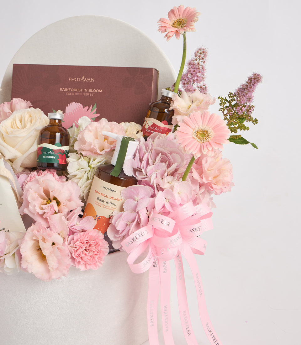 Luxurious Phutawan spa gift set with pink and cream flowers, amber bottles, body lotion, and burgundy box against white circular background.