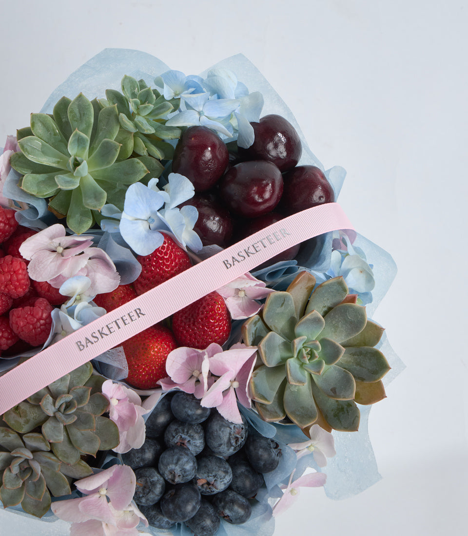 # Alt Text:

Luxury gift basket with fresh berries, succulents, hydrangeas, and pink ribbon labeled "BASKETEER" on white tissue paper background.