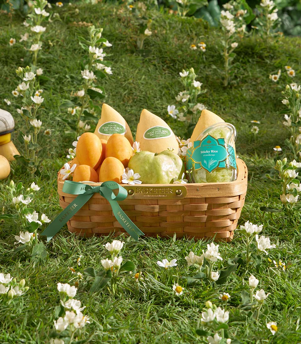 Luxury gift basket with golden mangoes, green guava, sticky rice, and Nam Dok Mai Sri Thong packages, tied with dark green