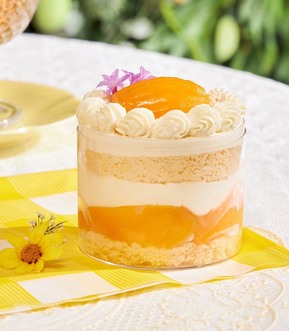 Light chiffon cake with fresh cream and fruit compote in clear cup, garnished with orange slice and edible flowers
