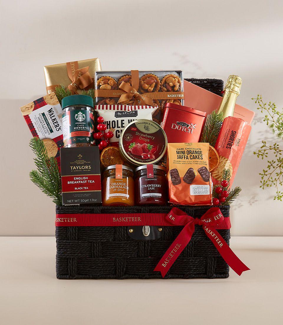 Dark woven luxury gift basket with red ribbon bow filled with gourmet treats, sparkling wine, and festive berries for New
