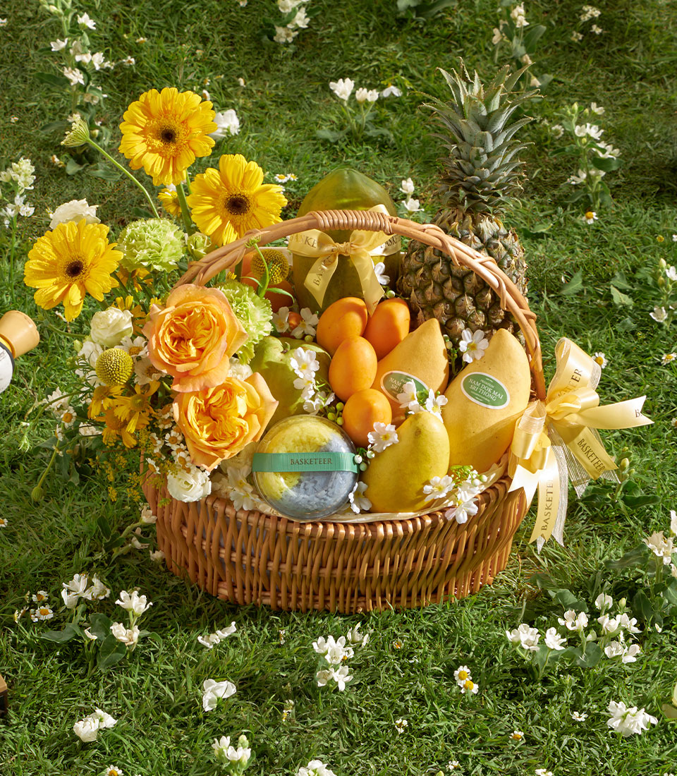 Sunlit Mango Garden gift basket with Nam Doc Mai mangoes, pineapple, papaya, and yellow gerbera daisies on green grass