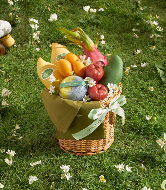 Compact wicker gift basket with fresh tropical fruits, yellow mangoes, dragon fruit, and rose apples on green lawn
