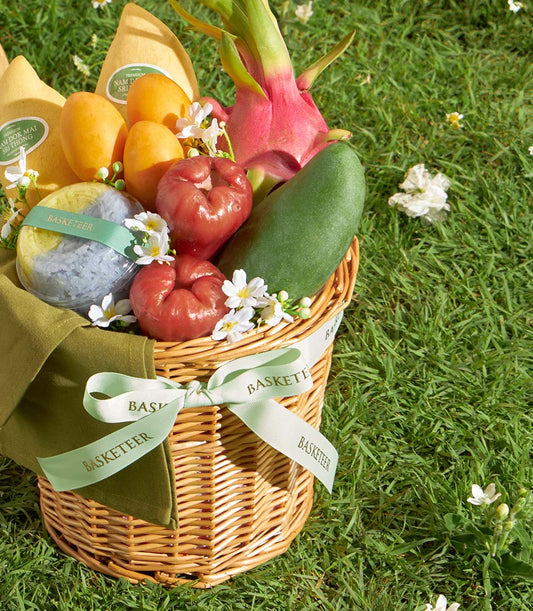 Woven wicker basket filled with fresh yellow mangoes, pink dragon fruit, rose apples, and artisan sticky rice dessert with