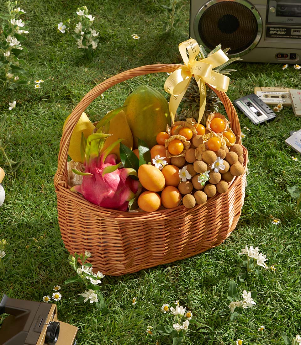 Premium Thai tropical fruit basket with papaya, mango, dragon fruit, and longan in wicker with yellow ribbon