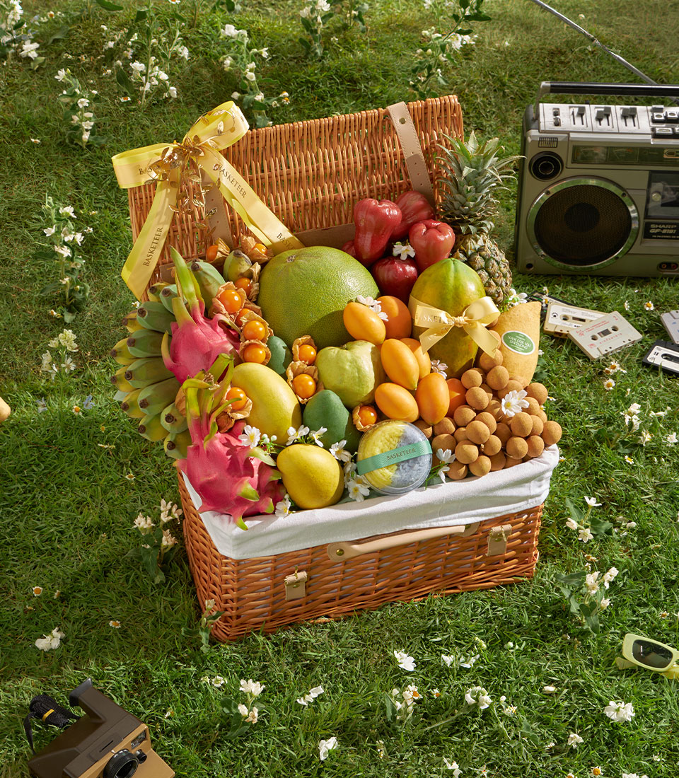 Luxury wicker hamper overflowing with tropical fruits—mango, pomelo, longan, dragon fruit, and pineapple—tied with yellow