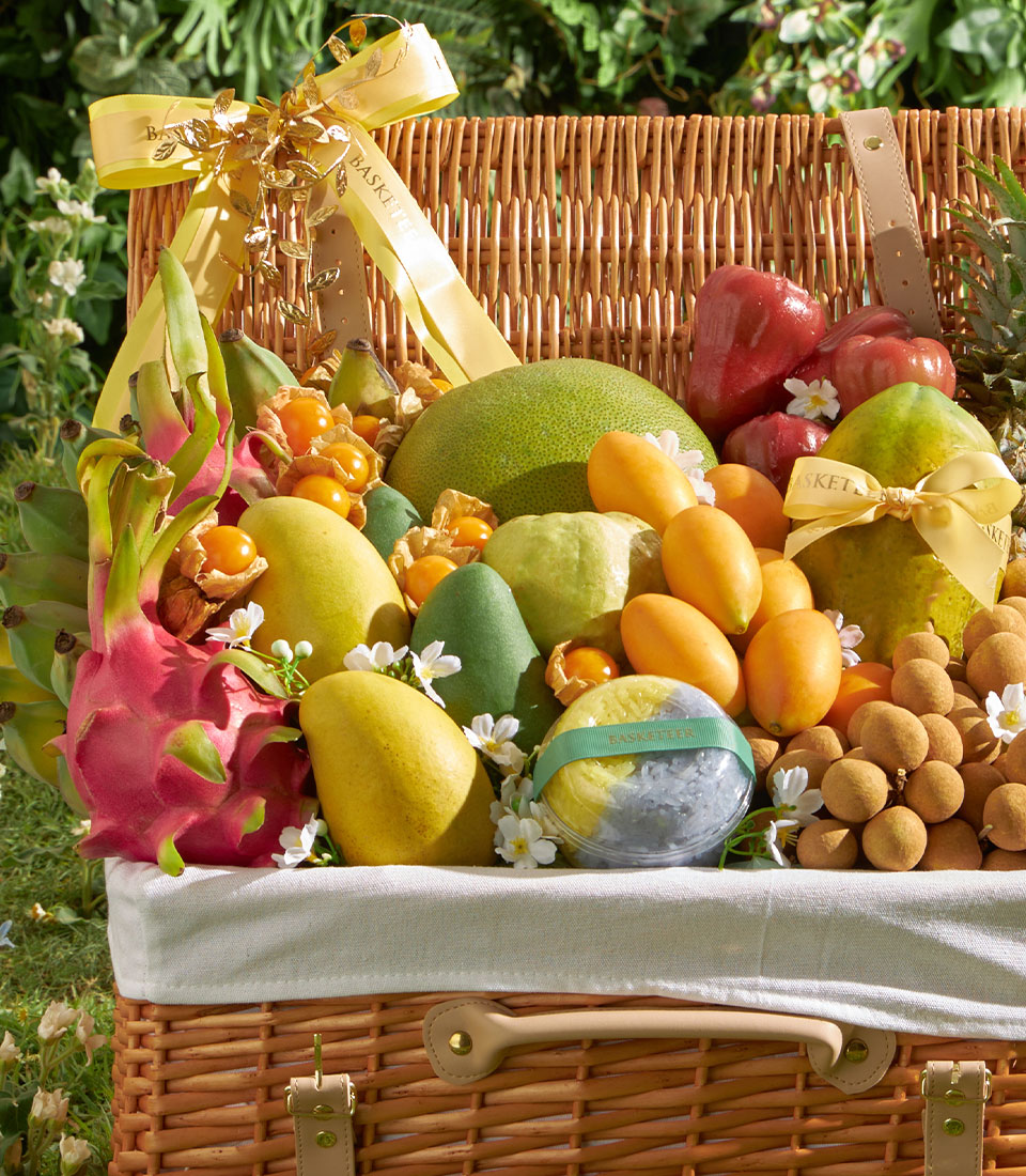 Luxury wicker hamper overflowing with fresh tropical fruits: mango, pomelo, longan, dragon fruit and guava