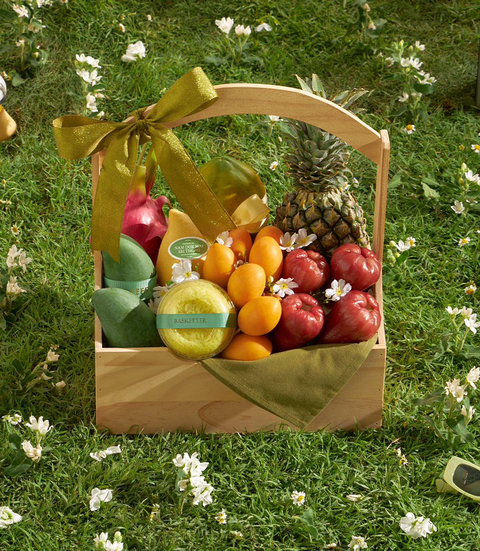 Wooden fruit basket with fresh mangoes, dragon fruit, papaya, pineapple, and rose apples tied with gold ribbon