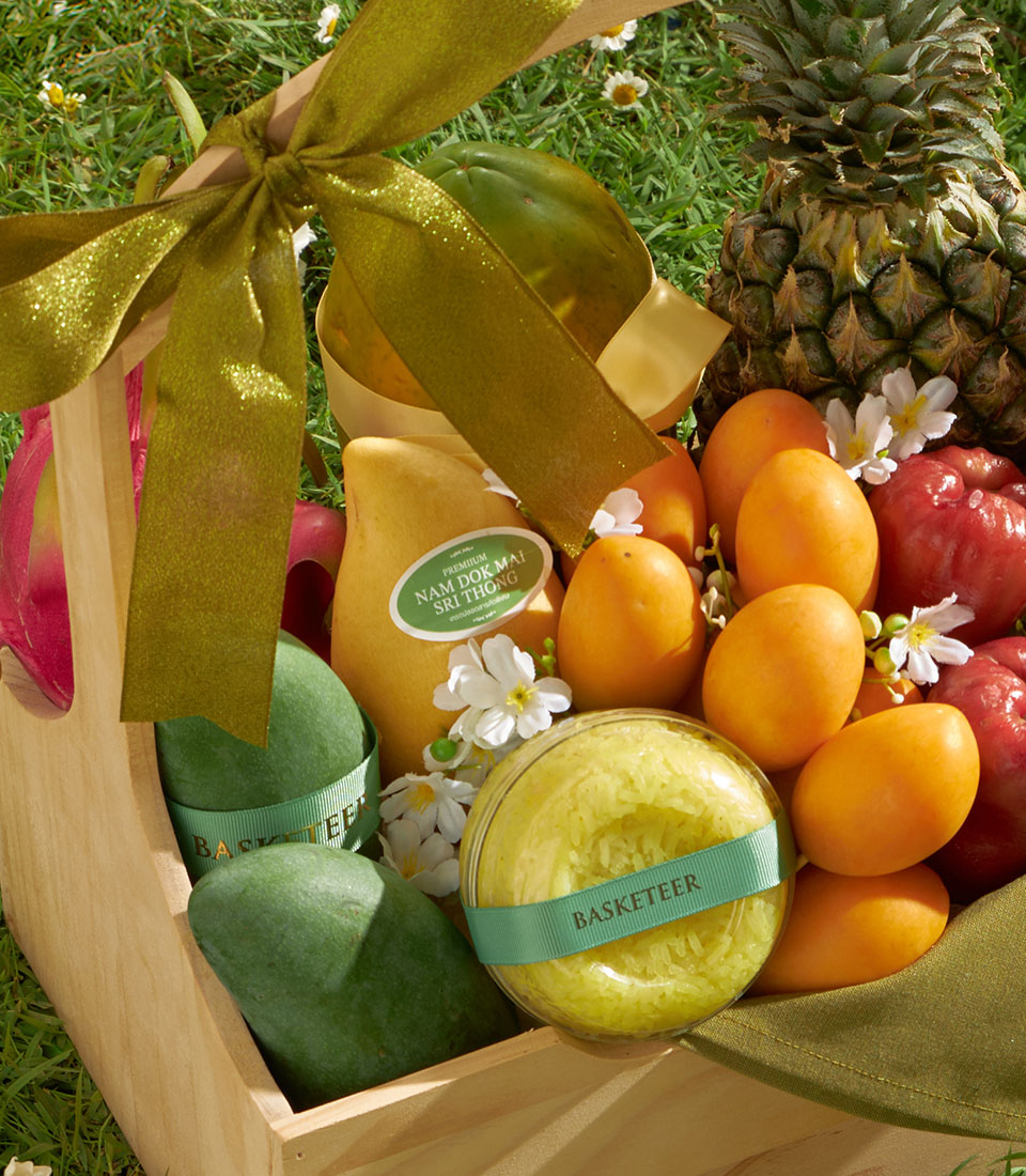 Wooden gift basket with fresh tropical fruits, premium Nam Dok Mai mango, pineapple, and roses apples on green grass
