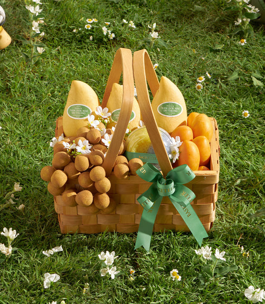 Woven wooden basket with premium Nam Doc Mai mangoes, longans, and tropical fruits on green grass