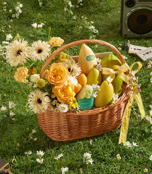 Golden mango and tropical fruit gift basket with sticky rice, fresh flowers, and yellow ribbon on green lawn