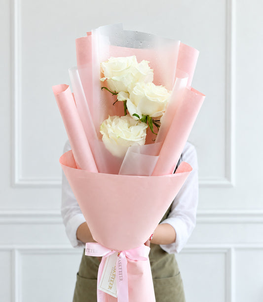 Three elegant white Mondial roses form a romantic bouquet, beautifully wrapped in soft pink paper