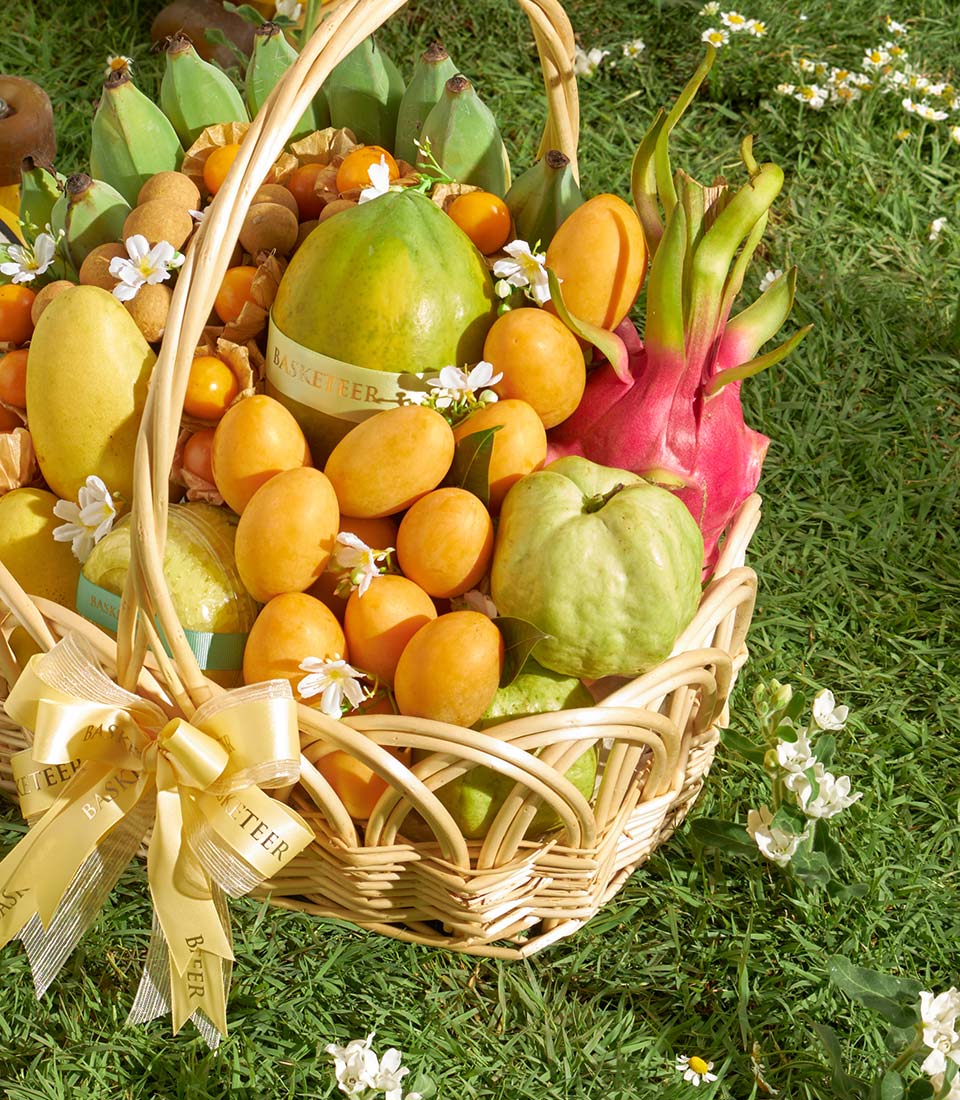 Premium woven basket filled with fresh Thai tropical fruits including mango, papaya, dragon fruit, and guavas with golden