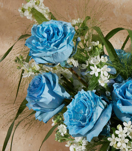 Light blue roses with white filler flowers and green foliage in a fresh vase arrangement