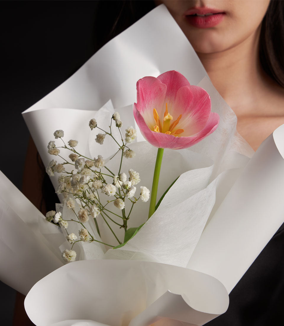 Elegant tulip bouquet from Flowers by Basketeer, featuring a single pink tulip and delicate white gypsophila, wrapped in crisp white paper. Flower delivery Bangkok.