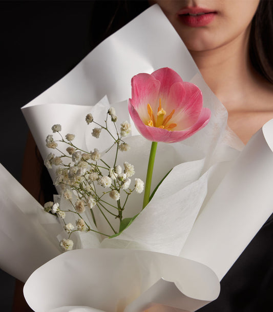 Elegant tulip bouquet from Flowers by Basketeer, featuring a single pink tulip and delicate white gypsophila, wrapped in crisp white paper. Flower delivery Bangkok.