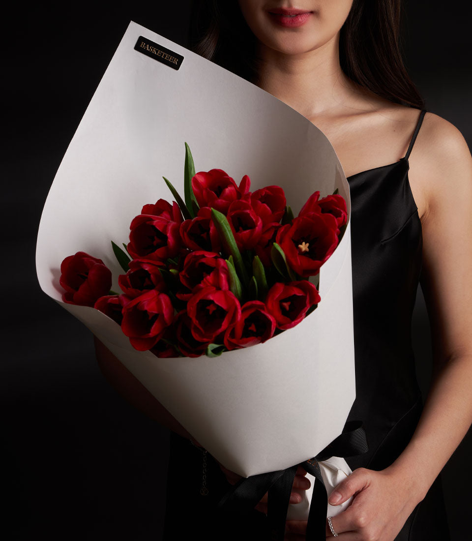 Red tulip Valentine bouquet with white paper wrap and black satin ribbon, held by woman in black dress