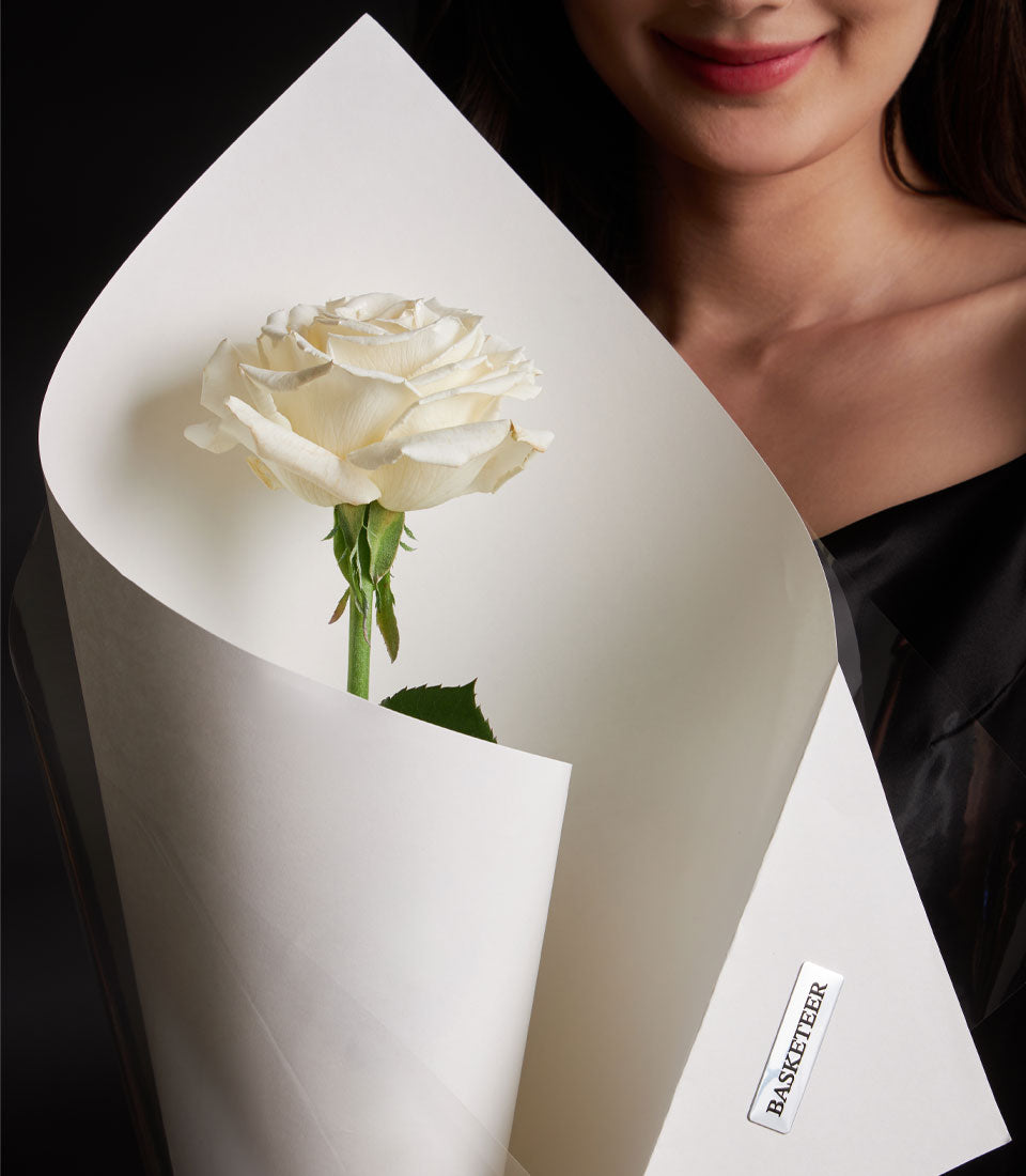 Single white rose wrapped in paper, held for Valentine's Day gift from Flowers by Basketeer
