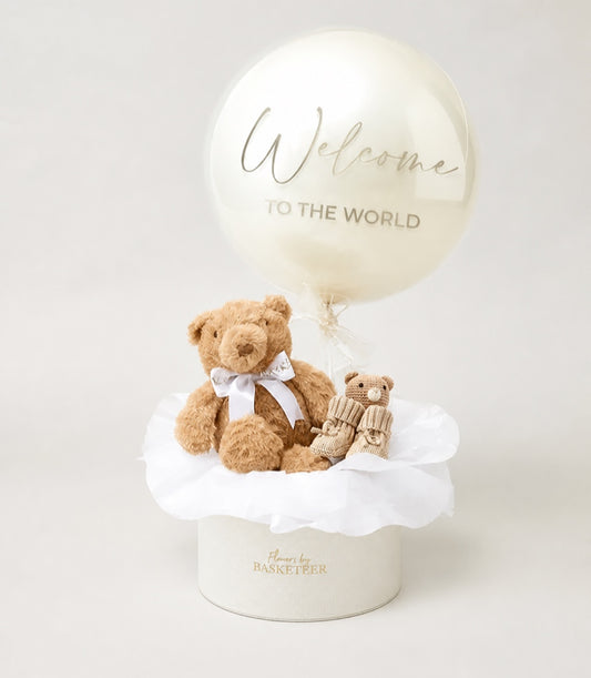 Basketeer luxury baby welcome gift hamper in a cream round box, featuring