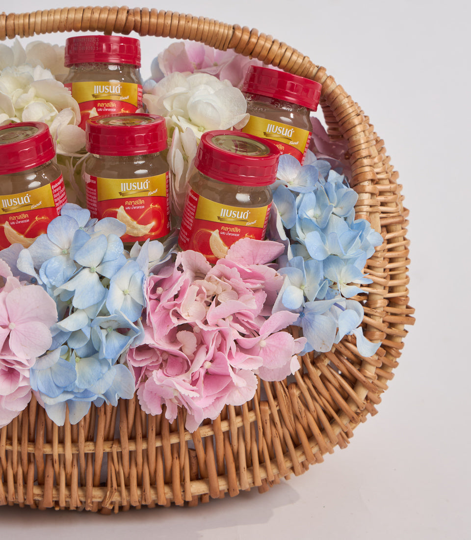 Wicker basket filled with colorful hydrangeas in pink, blue and white, decorated with red and gold labeled glass jars of Thai ginseng supplement product.