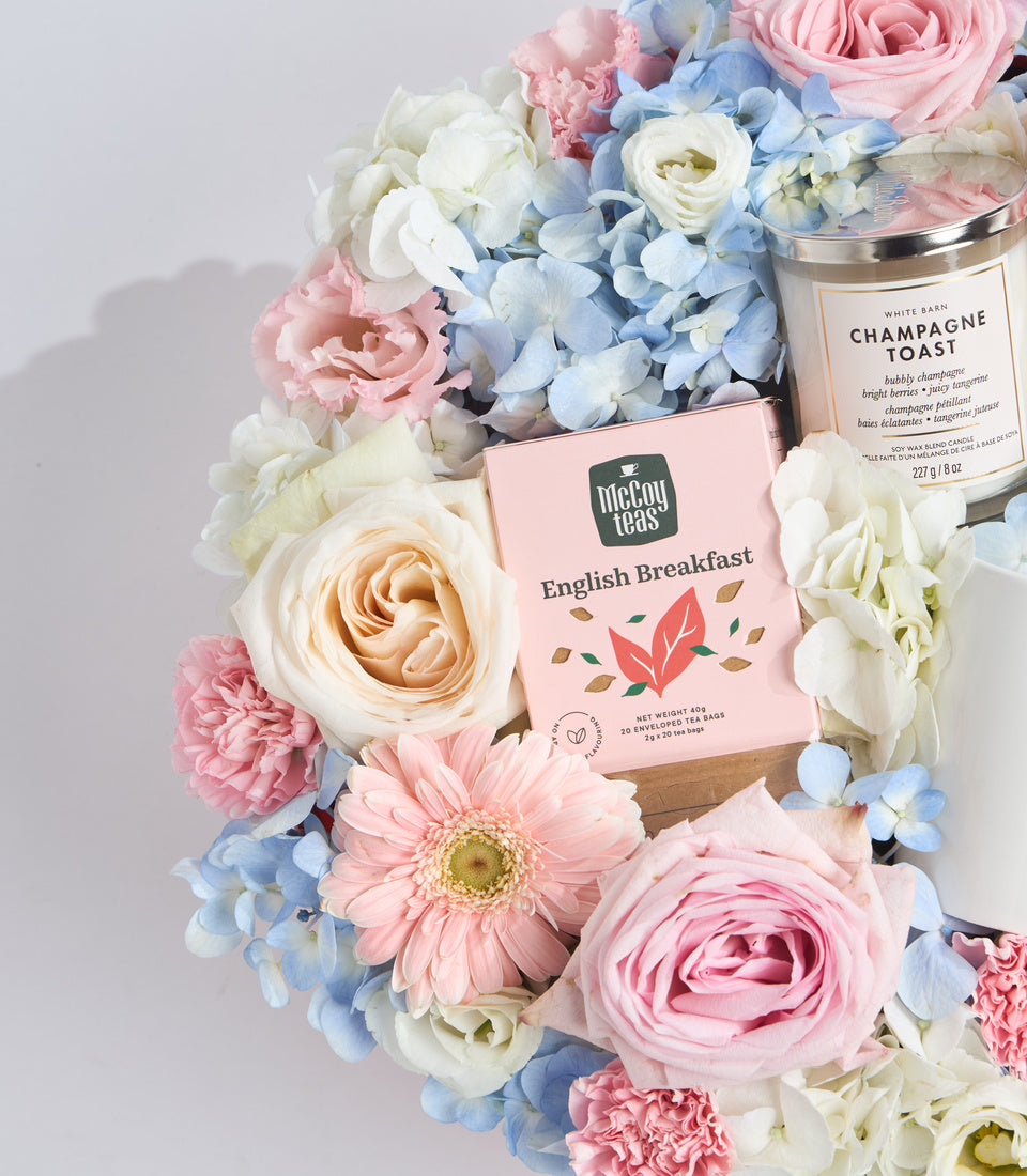 # Alt Text

Luxury gift set with pink McCoy Teas English Breakfast tea box, White Barn Champagne Toast candle, surrounded by fresh pink, white, and blue flowers on neutral background.