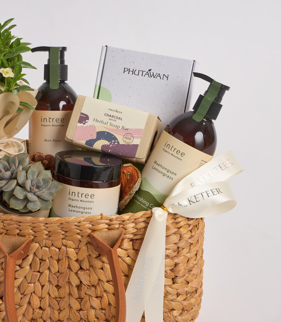 Organic skincare gift set in woven basket featuring brown glass bottles, charcoal soap bar, succulents, and white product packaging with natural, earthy aesthetic.