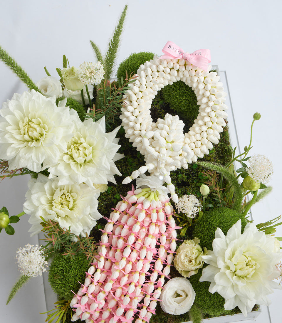# Alt Text

Luxurious floral arrangement featuring white dahlias, pink waxflower, moss spheres, and decorative pearl wreath with pink ribbon bow in white box.