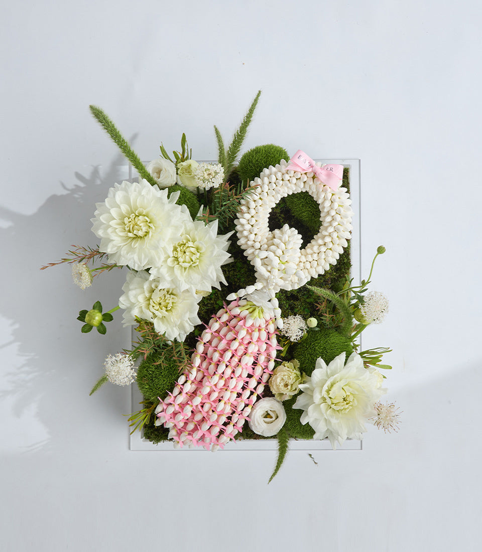 Elegant floral arrangement in white box featuring white dahlias, pink spray roses, white pearl beads, green moss, and decorative grasses with pink gift tag.