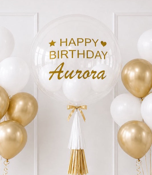 Elegant birthday balloon with gold text reading "Happy Birthday Aurora," surrounded by white and gold balloons with gold tassel decoration on white paneled background.