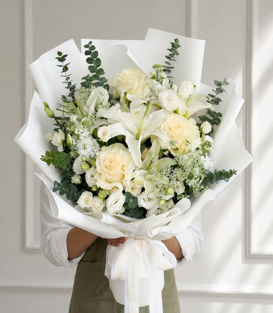 Elegant white rose and lily bouquet with lush green eucalyptus, beautifully wrapped in white paper