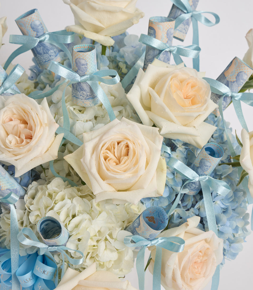 Elegant floral bouquet with cream roses, white hydrangeas, and blue silk ribbons with decorative royal portrait wrapping.